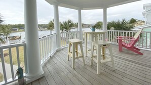 A covered porch with white railings, a table, two stools, and a red chair. - "Haven By The Sound" - Intercoastal Waterway Home w/ Pool, 6 Bedrooms / 6.5 Bathrooms (Holden Beach)