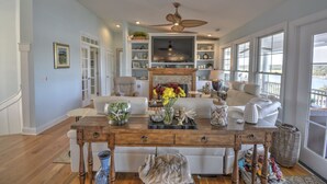 A spacious living room with a fireplace, a dining table, and a large TV. - "Haven By The Sound" - Intercoastal Waterway Home w/ Pool, 6 Bedrooms / 6.5 Bathrooms (Holden Beach)