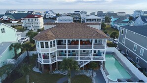 A coastal residential area with a prominent two-story house featuring a balcony, a swimming pool, and a view of the ocean. - "Haven By The Sound" - Intercoastal Waterway Home w/ Pool, 6 Bedrooms / 6.5 Bathrooms (Holden Beach)