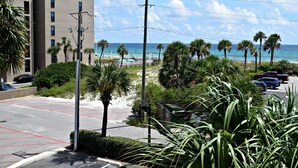A parking lot with marked spaces, a building with multiple windows, and a view of the beach with palm trees and the ocean.