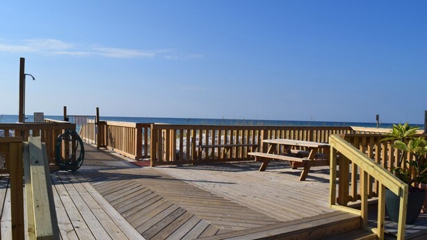 A wooden deck with a picnic table and a railing overlooking the ocean.