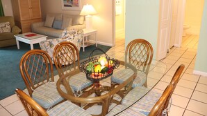 A dining area with a glass table surrounded by wicker chairs, a wicker sofa, and a lamp on a side table.
