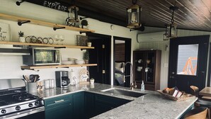 A modern kitchen with a central island, stainless steel appliances, and wooden accents. - Camp HighBridge 2 Bed 1 Bath Big Manistee River, Private Frontage. Bunk House! (Wellston)