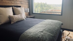 A bed with a patterned bedspread, two pillows, and a nightstand with a lamp. - Camp HighBridge 2 Bed 1 Bath Big Manistee River, Private Frontage. Bunk House! (Wellston)
