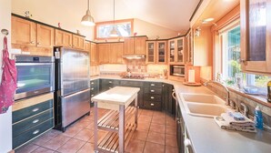 Une cuisine moderne dotée de meubles en bois, d’appareils électroménagers en acier inoxydable, d’un îlot central et d’une grande fenêtre qui laisse entrer la lumière naturelle.