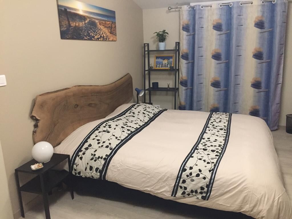 Ein Schlafzimmer mit einem hölzernen Kopfteil, einem Bett mit einer weiß-schwarz gemusterten Tagesdecke, einem Nachttisch mit Lampe und einem Regal mit dekorativen Gegenständen.