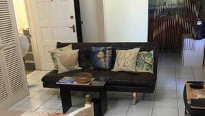 A living room with a sofa, coffee table, and a bed. There is a door and a window with curtains. - 1 Bed Villa - Sleeps 2 - Garden - Parking - Wifi (Ocho Rios)