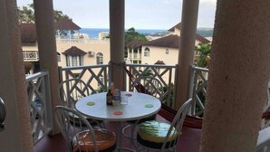 A balcony with a round table and chairs, overlooking a coastal area with buildings and trees. - 1 Bed Villa - Sleeps 2 - Garden - Parking - Wifi (Ocho Rios)