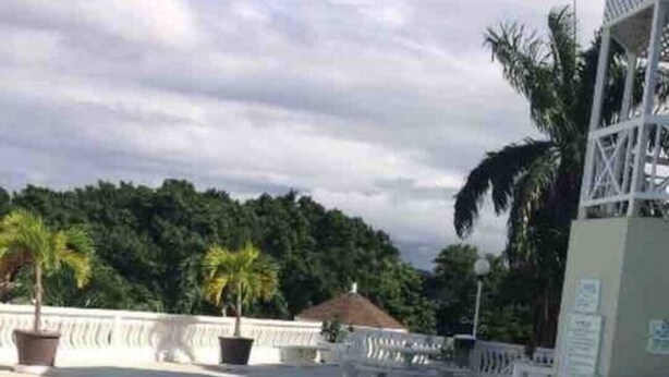 A swimming pool with clear blue water, surrounded by a white fence and palm trees. - 1 Bed Villa - Sleeps 2 - Garden - Parking - Wifi (Ocho Rios)