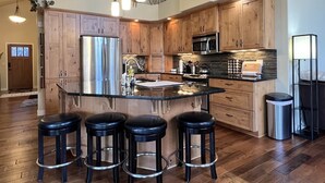 A spacious kitchen with wooden cabinets, stainless steel appliances, and a central island with stools. - Cp20 The Perfect Glacier Getaway (Columbia Falls)