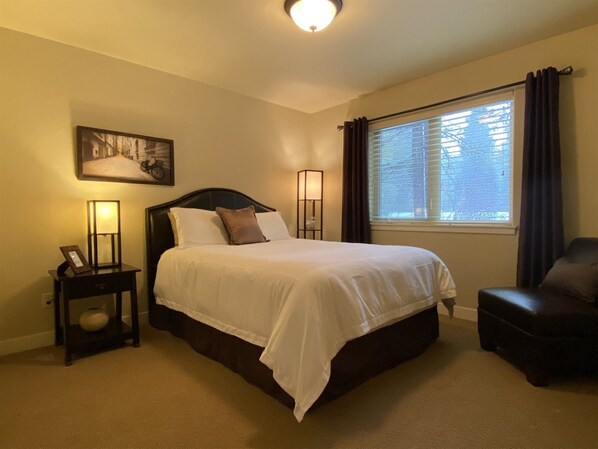 A neatly arranged bedroom with a large bed, a bedside table with a lamp, a chair, and a window with curtains. - Cp20 The Perfect Glacier Getaway (Columbia Falls)