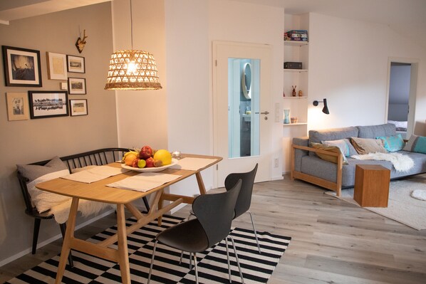 Un soggiorno moderno con zona pranzo, che include un tavolo in legno, un tappeto a righe bianco e nero e un divano grigio. Si nota una porta blu sullo sfondo.