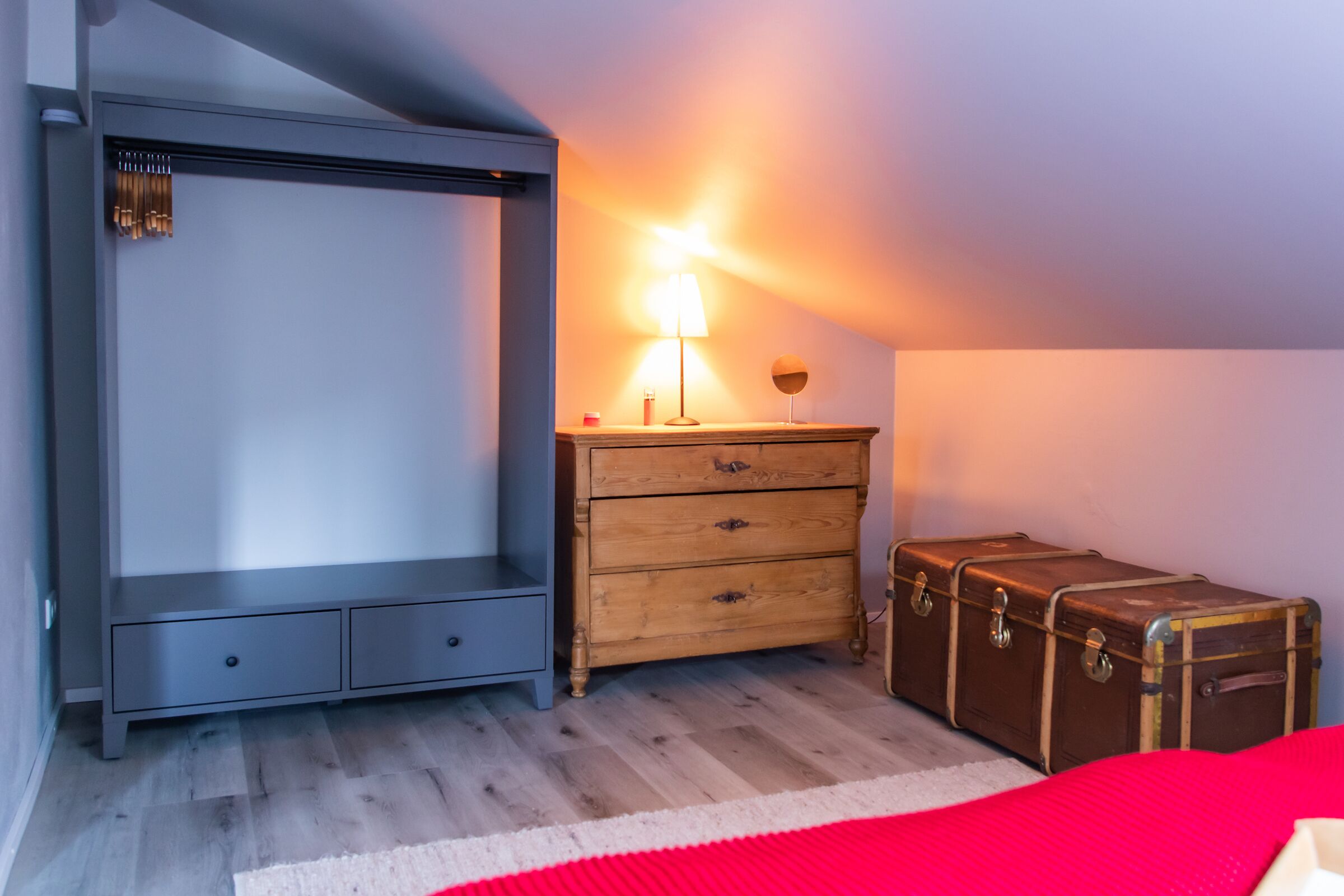 Une chambre à coucher avec un lit, une commode, une lampe et une valise.