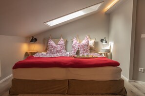 Una camera da letto con un lucernario, un letto con coperta rossa, due comodini con lampade e un vassoio con oggetti sul letto.