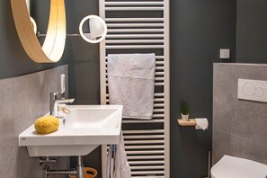 Un bagno moderno con lavandino bianco, specchio, porta asciugamani e water.