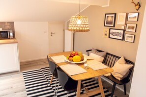 Zona pranzo con tavolo in legno, sedie nere, tappeto a righe bianco e nero, una ciotola di frutta e un lampadario.