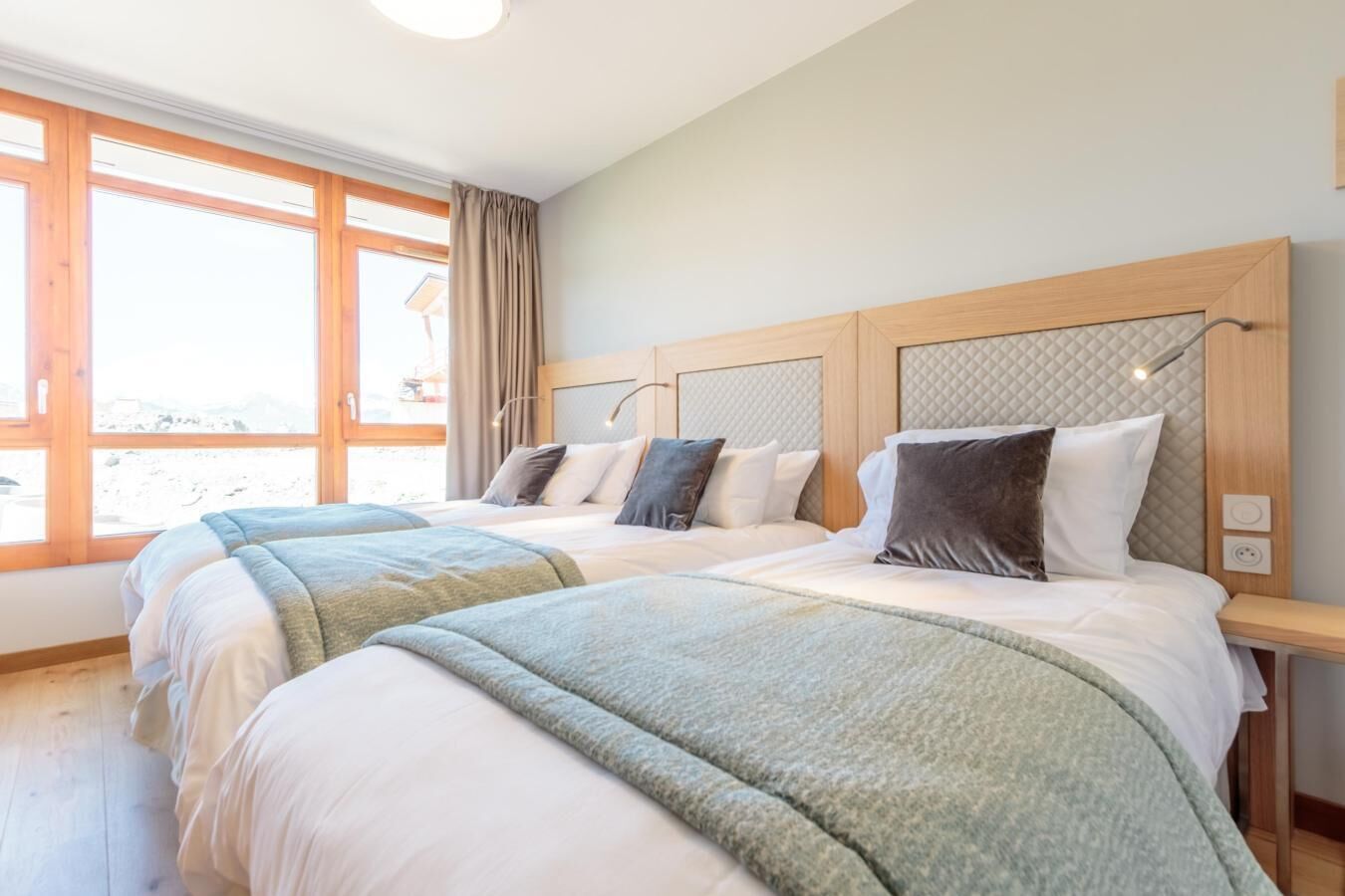 A hotel room with a large window, two beds with matching headboards, and a wooden nightstand.
