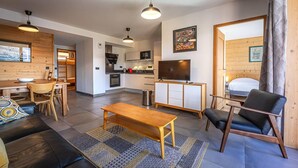 A modern living room with a sofa, a wooden coffee table, and a TV. There is a kitchen area with a microwave and a dining table. - 100m from ski slopes, floor -1, view valley, fitness, sauna, hammam, terrace, parking, tv (Bourg-Saint-Maurice)