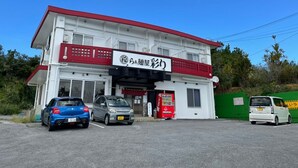 A two-story building with a red and white facade, a sign with Japanese characters, and a vending machine in front. - Nago Sakura Resort Inn (名護市)