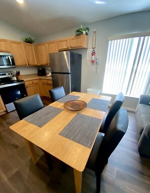 A modern kitchen with wooden cabinets, stainless steel appliances, and a dining table with black chairs.