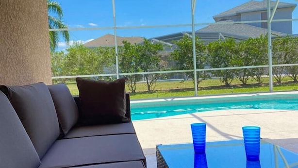 A covered outdoor seating area with a view of a swimming pool and greenery. - Remington Family Fun Comfort & Sunshine – 4BR Villa w/ Pool (Osceola County)
