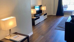 A modern living room with a flat-screen TV, two lamps, a sofa, and a rug. - Remington Family Fun Comfort & Sunshine – 4BR Villa w/ Pool (Osceola County)