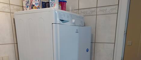 A compact laundry area with stacked appliances, including a washing machine and a dryer, in a room with tiled walls and a tiled floor.