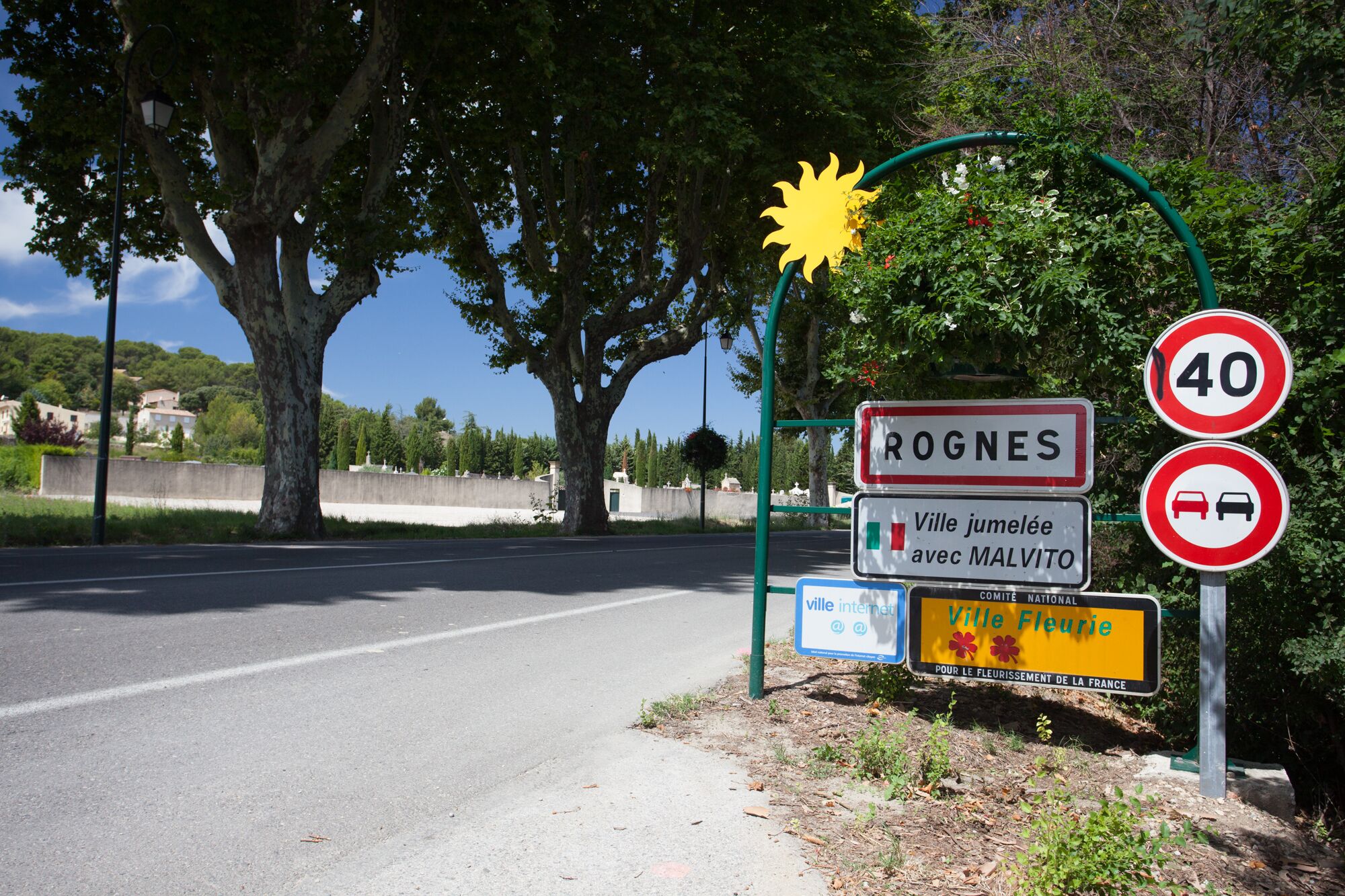 Tienvarsikyltti, jossa lukee »ROGNES» ja »Ville Fleurie», osoittaa kaupungin sijainnin, ja sen vieressä on nopeusrajoituskyltti, jossa lukee 40 km/h.