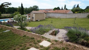 Una propiedad residencial con piscina, un edificio de piedra y un césped bien cuidado con plantas de lavanda.