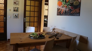 Comedor con una mesa de madera, sillas, un frutero y un cuadro de especias en la pared.