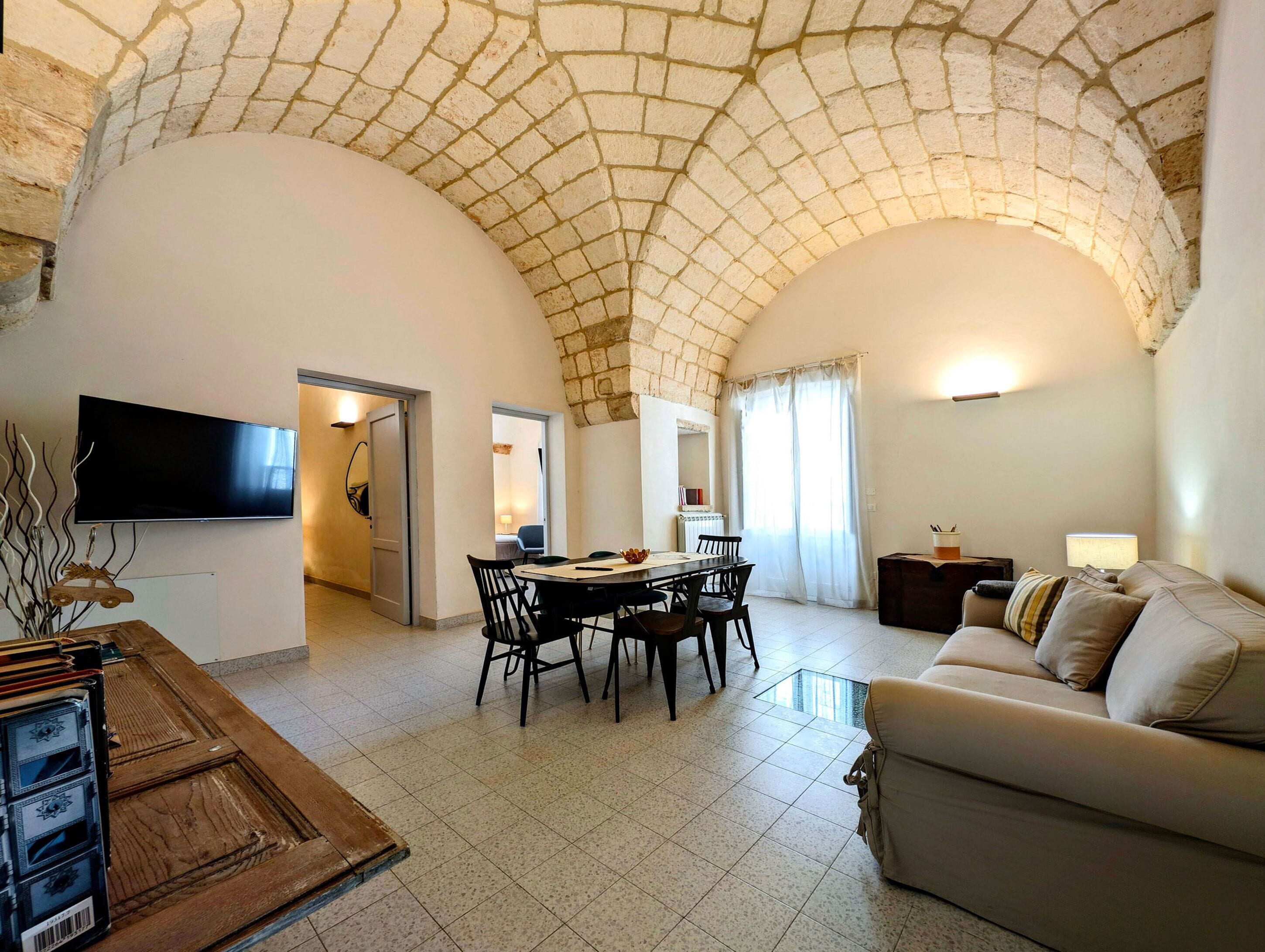 Un vaste espace de vie doté d’un haut plafond en arc de cercle, d’une table à manger avec des chaises, d’un canapé, d’un téléviseur à écran plat fixé au mur et d’une cheminée.