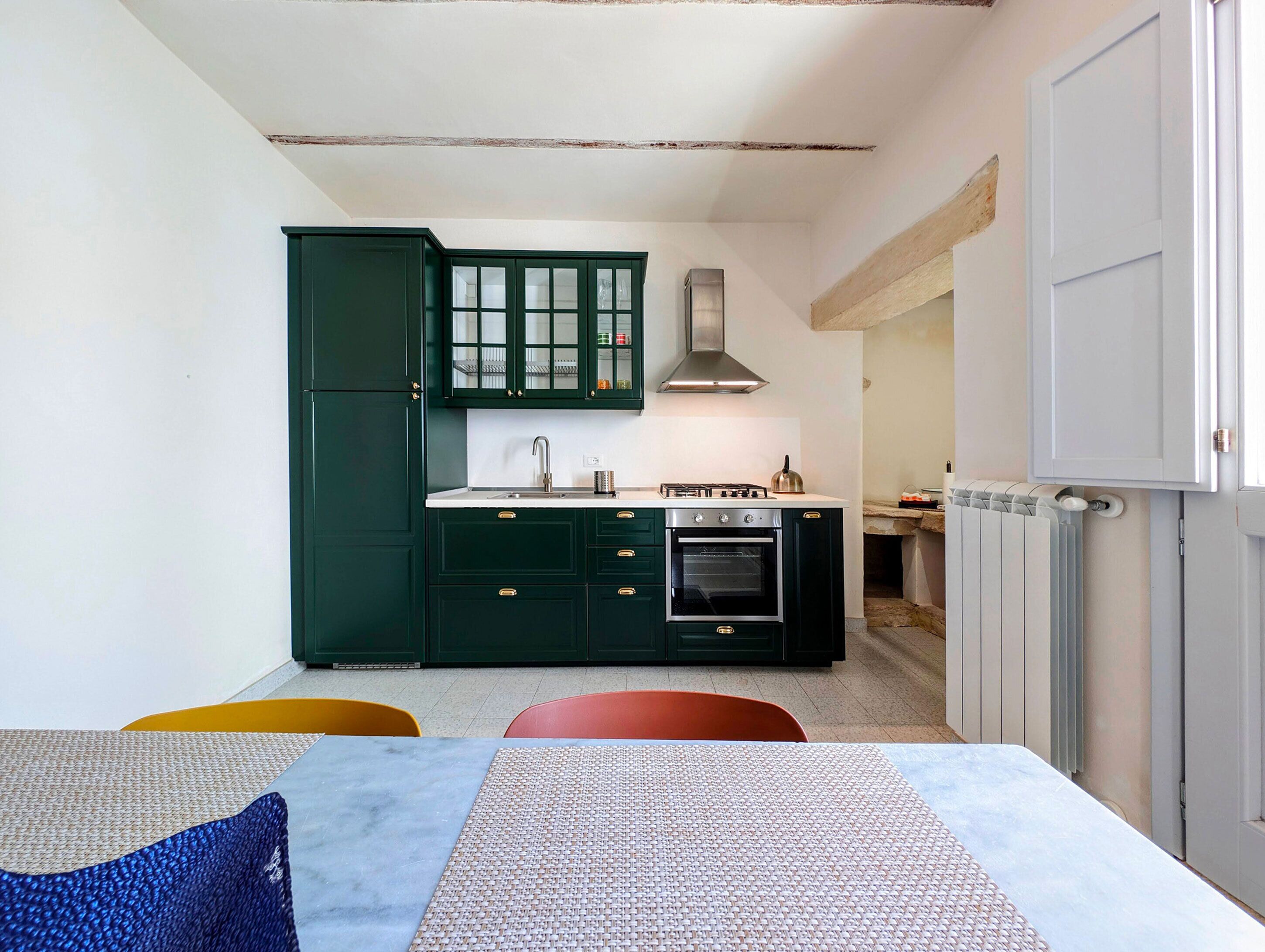 A compact kitchen with dark green cabinets, a white countertop, and a built-in oven.