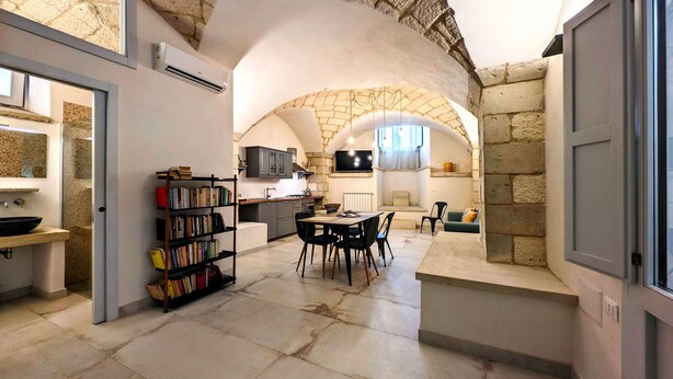 Una cocina amplia con un arco de piedra, un comedor con sillas y una estantería llena de libros.
