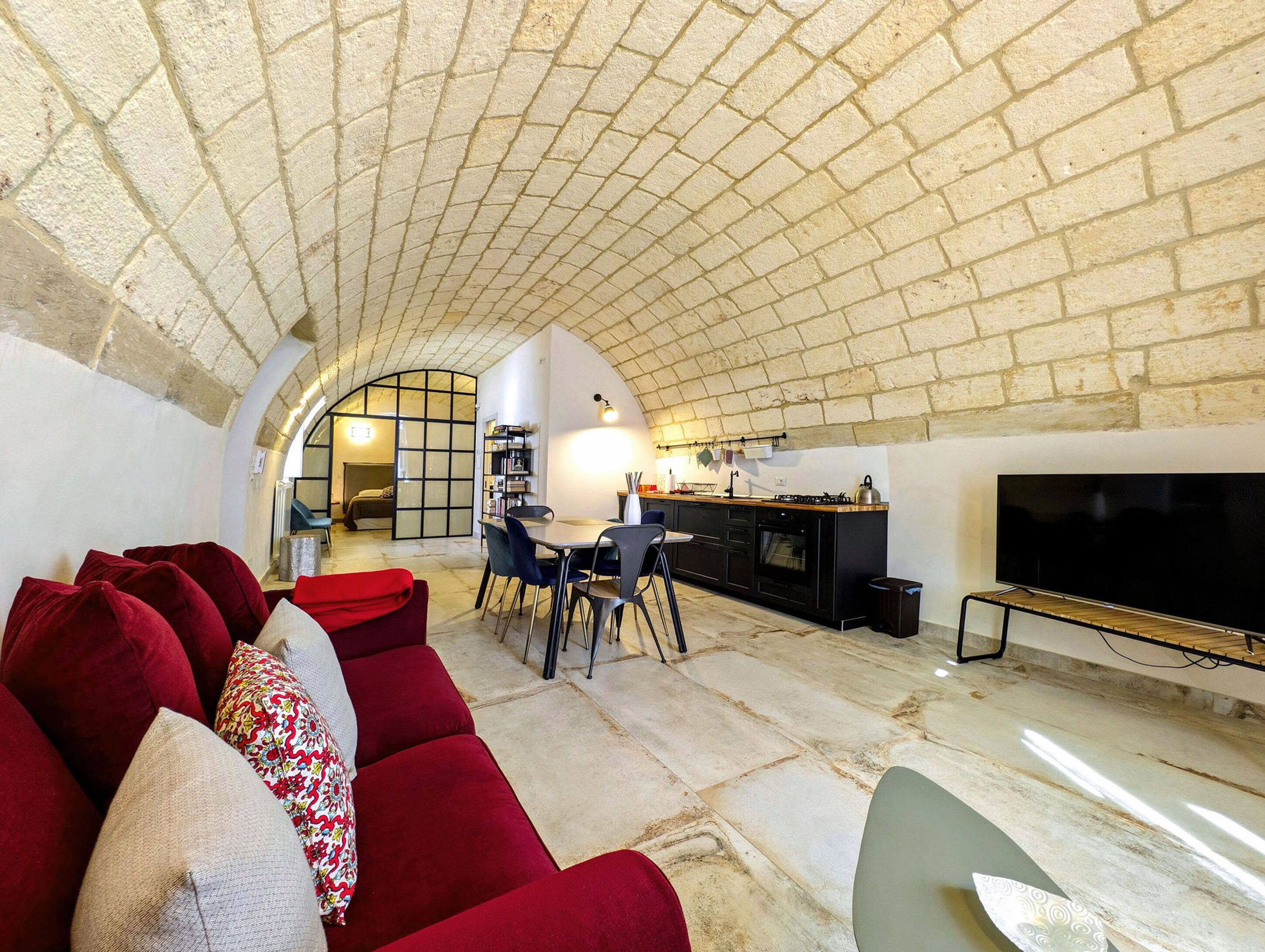 A cozy living room with a red sofa, a TV, and a kitchen area with a large window.