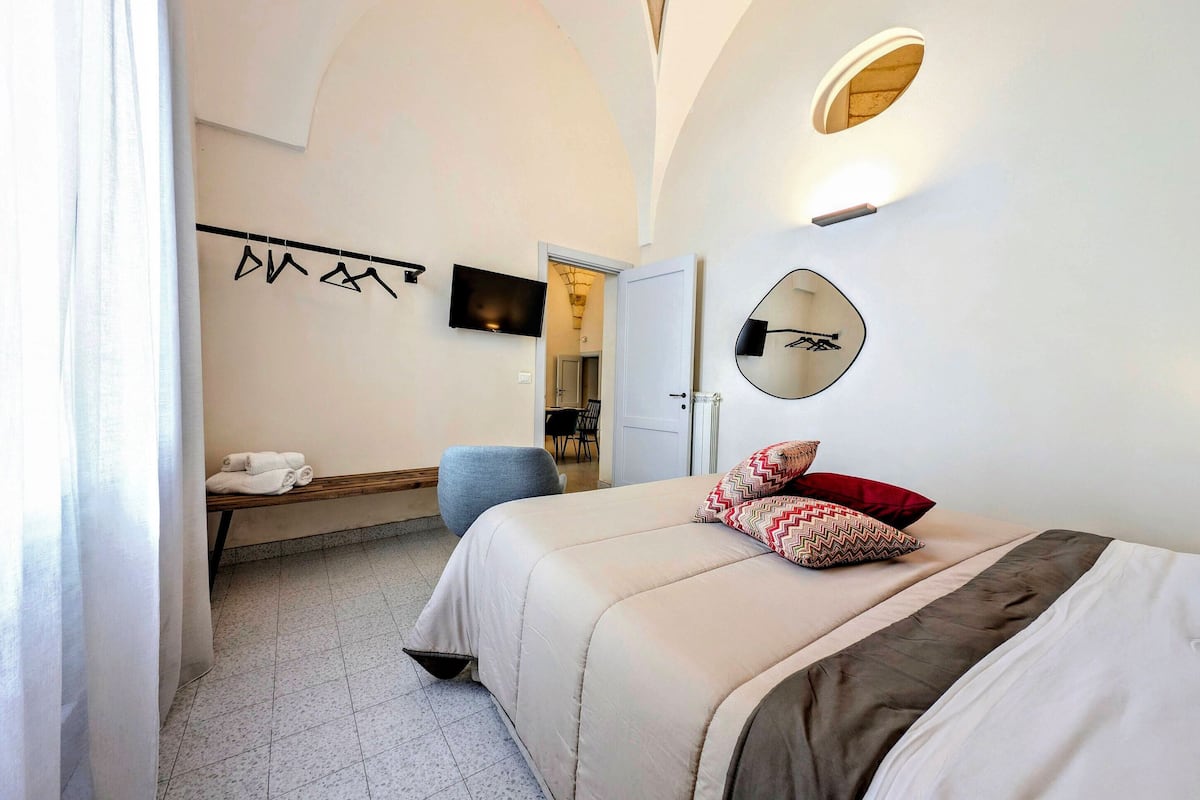 Una habitación de hotel moderna con una cama, un escritorio, una silla, un televisor y un espejo.