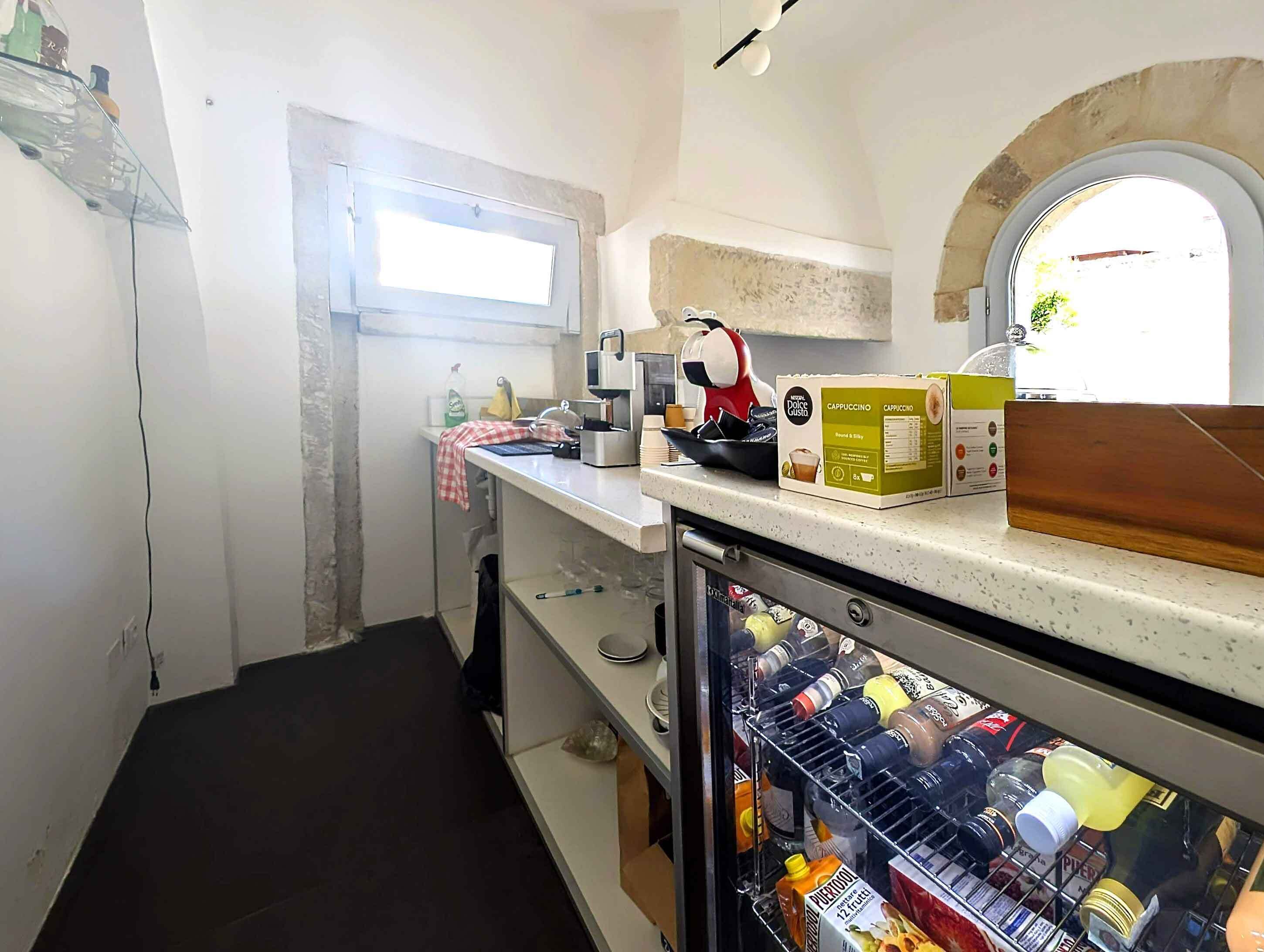 Una cocina con cafetera, un refrigerador lleno de bebidas y una ventana con vistas al exterior.