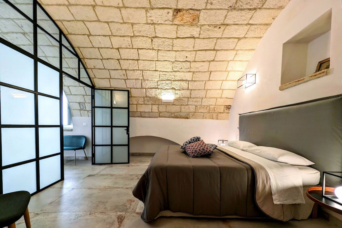 Un dormitorio con una cama grande, una silla y vistas a través de un ventanal.