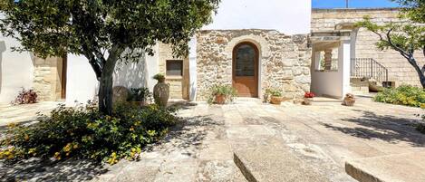 A courtyard with stone walls, a central archway, and potted plants.
