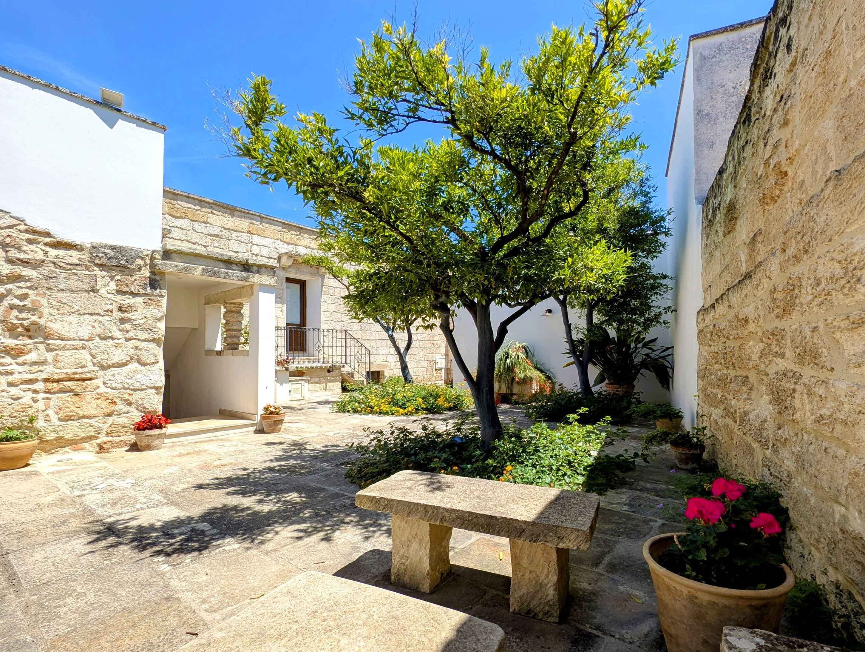 Un patio con muros de piedra, un banco y plantas en macetas.