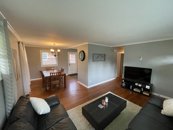 A living room with a sofa, coffee table, TV, and dining area with chairs and a table.
