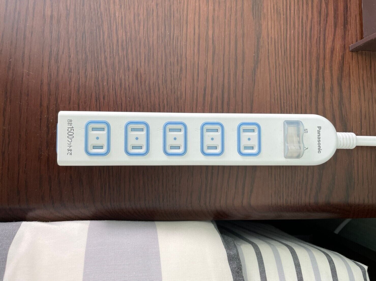 Una regleta blanca con cinco puertos USB y una pantalla, fijada a una superficie de madera.
