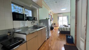 A compact kitchen with a microwave, sink, and stove, leading to a small dining area and a bedroom with a bed and a nightstand. - NAGO Sakura Resort Inn (Nago)