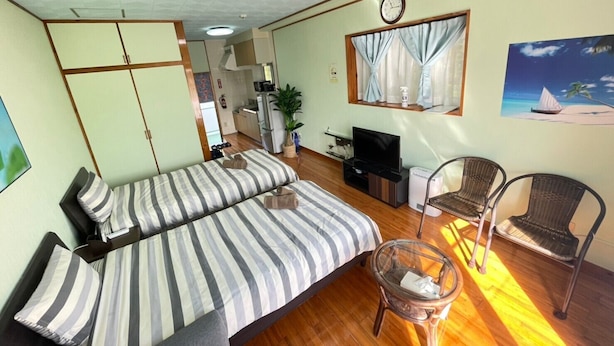 A room with a bed, two chairs, a TV, and a painting on the wall. - NAGO Sakura Resort Inn (Nago)
