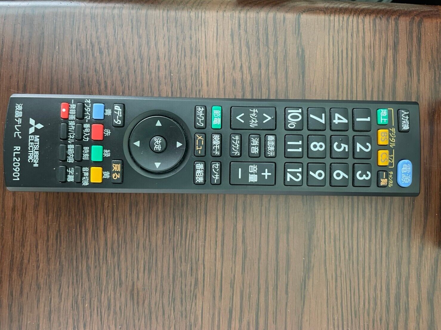 A black remote control with Japanese text and symbols, placed on a wooden surface.