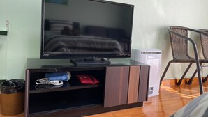 A television on a wooden stand in a room with a bed, a chair, and a trash bin. - NAGO Sakura Resort Inn (Nago)