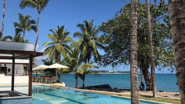 A pool area with lounge chairs, palm trees, and a view of the ocean.