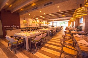 Un restaurante amplio con varias mesas y sillas, suelo de madera y lámparas colgantes.