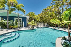 A swimming pool with a curved edge, surrounded by palm trees and a white fence. - Blue Lagoon (Anna Maria)