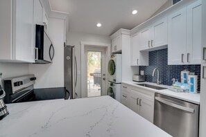 A modern kitchen with white cabinets, a stainless steel dishwasher, and a black and white marble countertop. - Blue Lagoon (Anna Maria)