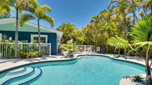A swimming pool with a curved edge, surrounded by palm trees and a building with a blue exterior. - Blue Lagoon North by SeaBreeze Vacation (Anna Maria)